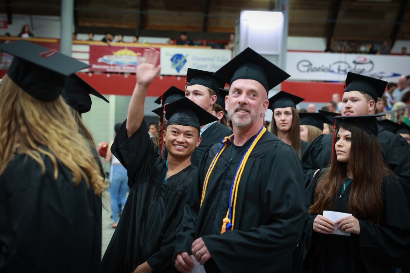 Photography and Design graduate Si Koch Koch of Marshall waves to his supporters in the audience as he enters the Ridgewater College commencement in Willmar. Beside him is Professional Photography graduate Mark Brendemuehl of Kerkoven, followed by Monserrat Soriano Alonso of Willmar.