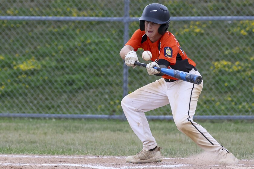 boys playing baseball outside in black and orange uniform and in black and red uniforms