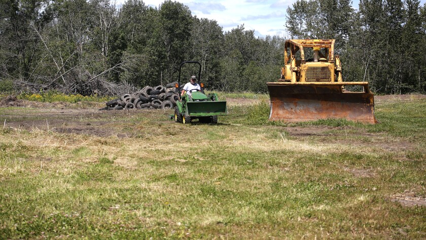 The man drives the tractor away as a big pile of thrown tires.
