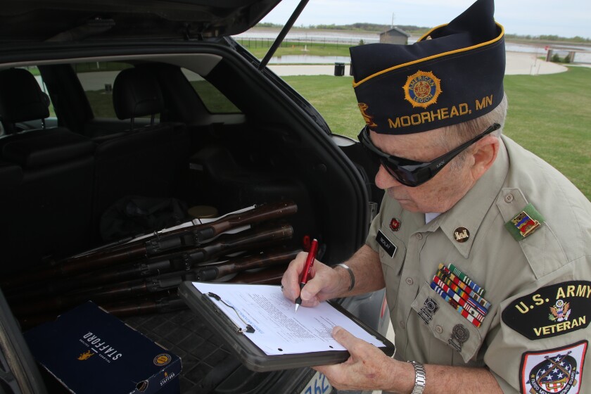 A man in sunglasses and a veteran's garrison cap fills out a form on a clipboard.