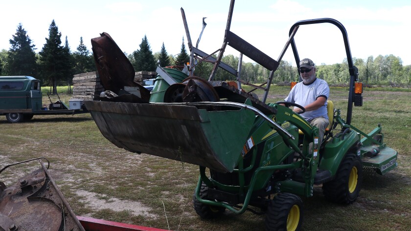Man riding a tractor unloads a large amount of junk onto a trailer.
