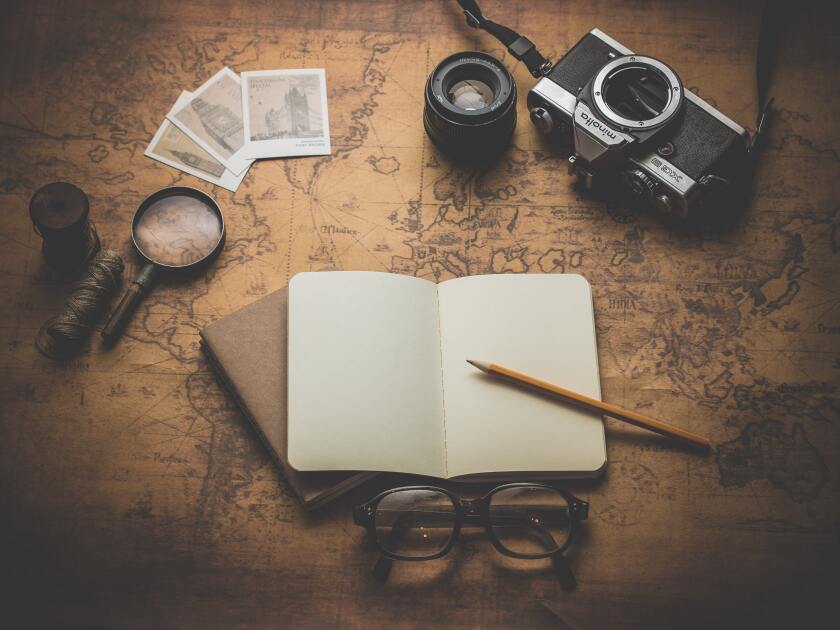 A diary sits above a map surrounded by a camera, a pair of glasses, photographs and a magnifying glass.