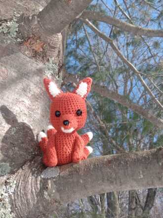 orange crocheted animal sitting on a tree branch