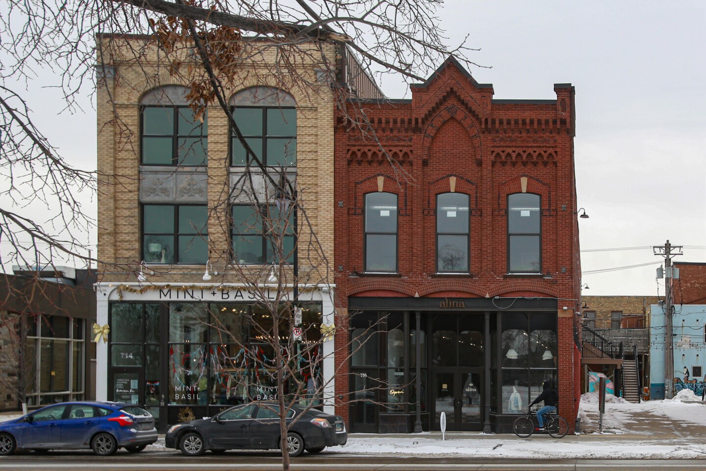 Alina Collective, as seen on Tuesday, Feb. 04, 2025, is located in the street-level retail space at 716 Main Ave. in downtown Fargo. Shown are two connected brick buildings. One is a three story building and the other is two stories with high ceilings. They have shops on the main floor. A person riding a bike is passing the buildings. The sky is overcast.