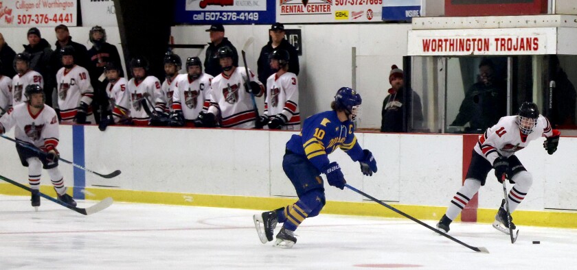 Worthington Trojans bench watches as Blake Ahrenstorff (11) skates into Blujays ice hotly pursued by Waseca defenseman Jarret Ahlschlager during Thursday night's game at the Worthington Ice arena.