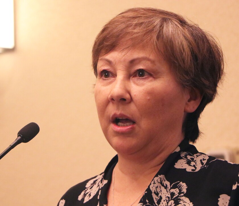 A woman speaks at a microphone in a hotel conference room.