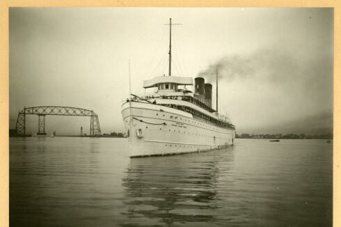 A black and white photo of  a ship in front of a bridge