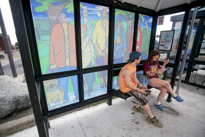 A man and woman sitting on a bench in a bus shelter that features a mural on the windows.
