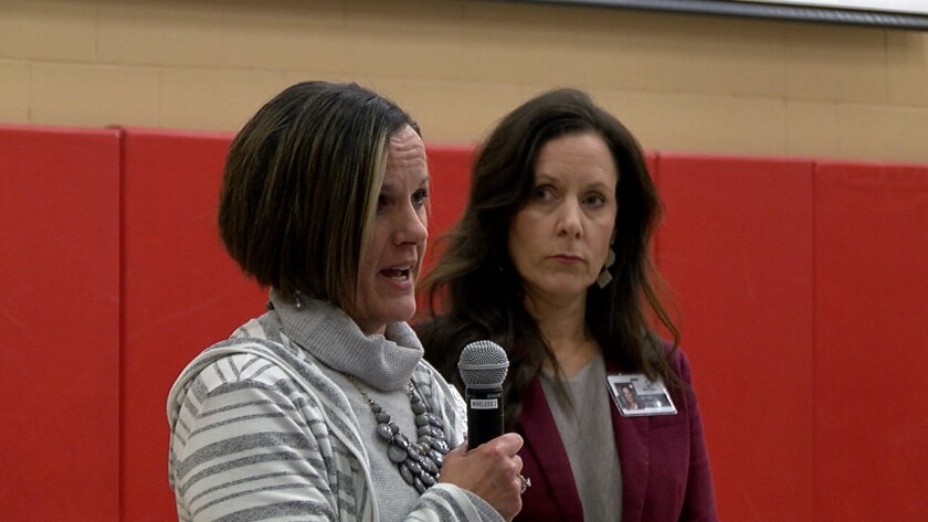 A woman holds a microphone as she speaks in a gymnasium