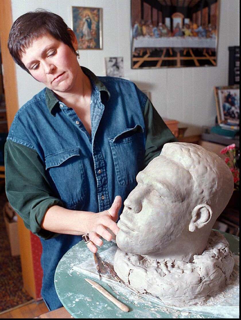 woman applies water to face of clay sculpture