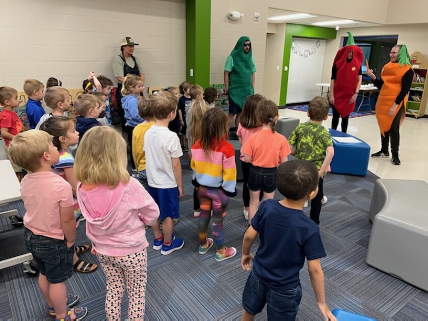 Children stand and listen to a presentation about vegetables from people in vegetable costumes.