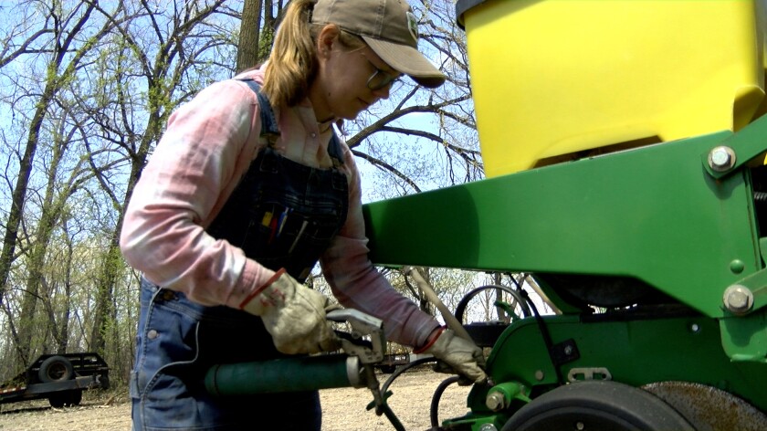 A woman dressed in a pink shirt and denim overalls greases the bearings on a green planter.