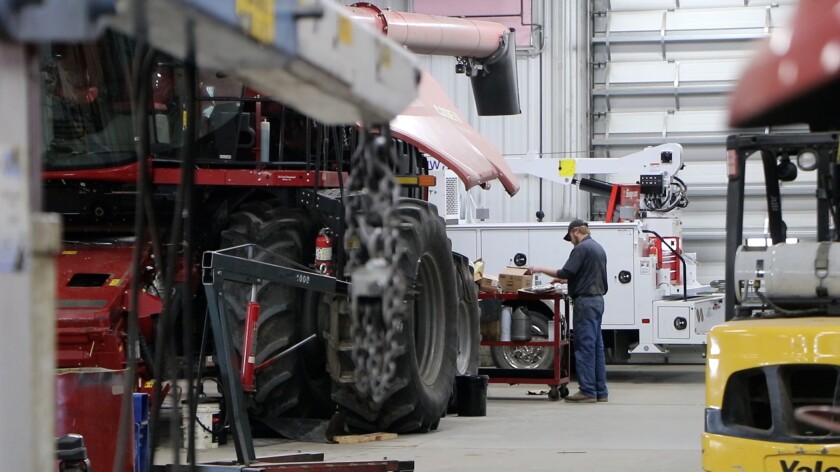 A technician stands amid a cavernous shop, with red Case-IH combines.