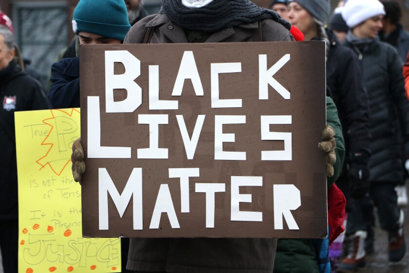 Person marching carries sign reading 'Black Lives Matter'.