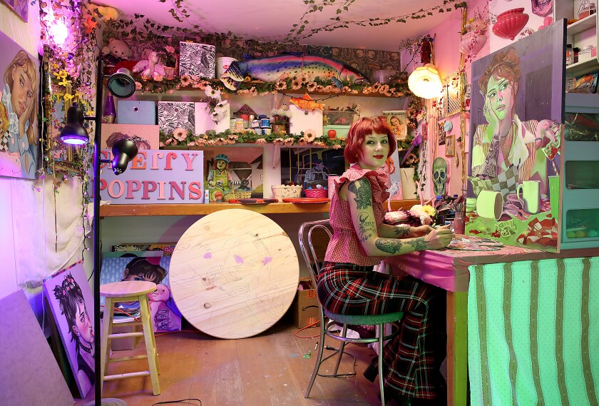 Artist Emily Koch is surrounded by some personal belongings and her paintings as she works in her studio space
