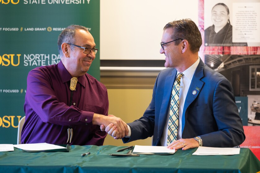 Two men sitting at a table and smiling while shaking hands