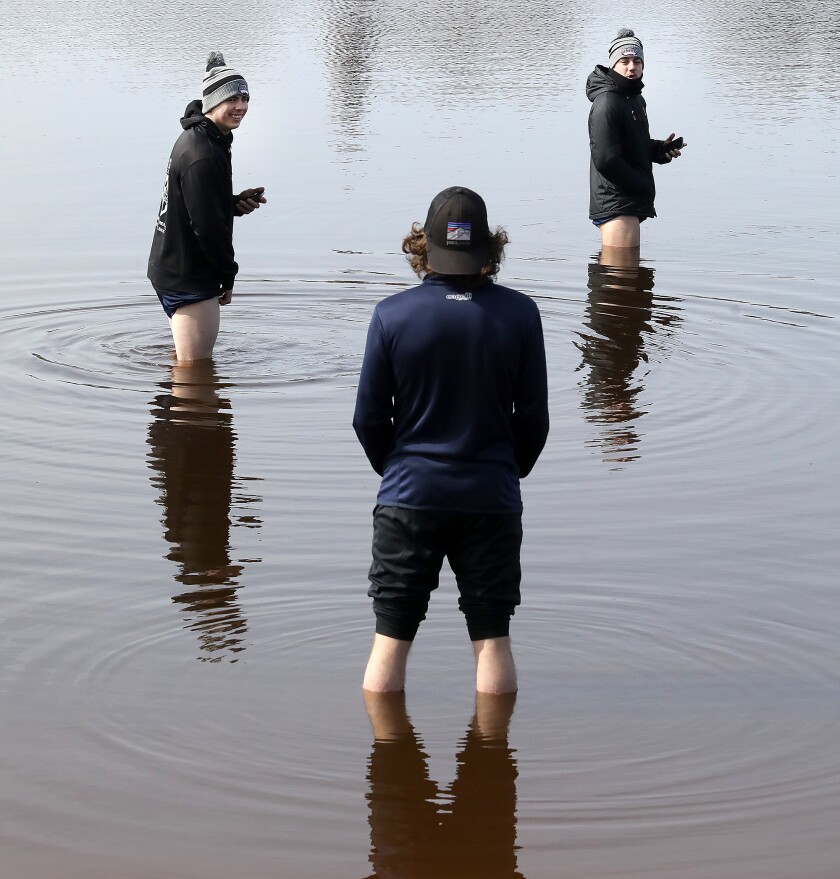 Alex Paredes, left, and Scott Wilson, right, chat with Blake Perry as they stand in the frigid waters of the Superior Bay