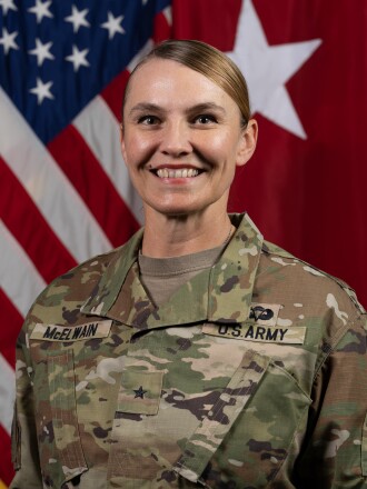 Smiling woman in combat uniform standing in front of a U.S. flag