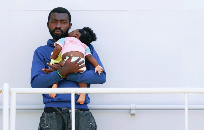 A migrant holds a baby as he waits to disembark from Italian Navy ship Sirio in the Sicilian harbour of Augusta, Italy, Aug. 21. REUTERS/Antonio Parrinello
