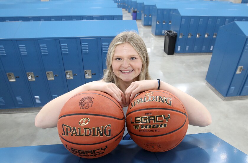 Basketball player leans on two basketballs on top of lockers.