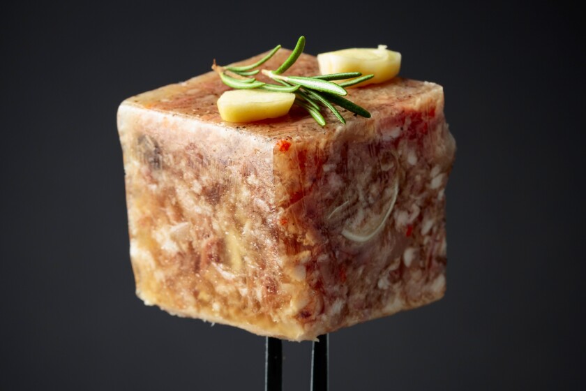 cube of gelatinous brown substance on fork, garnished with slices of garlic and rosemary sprig