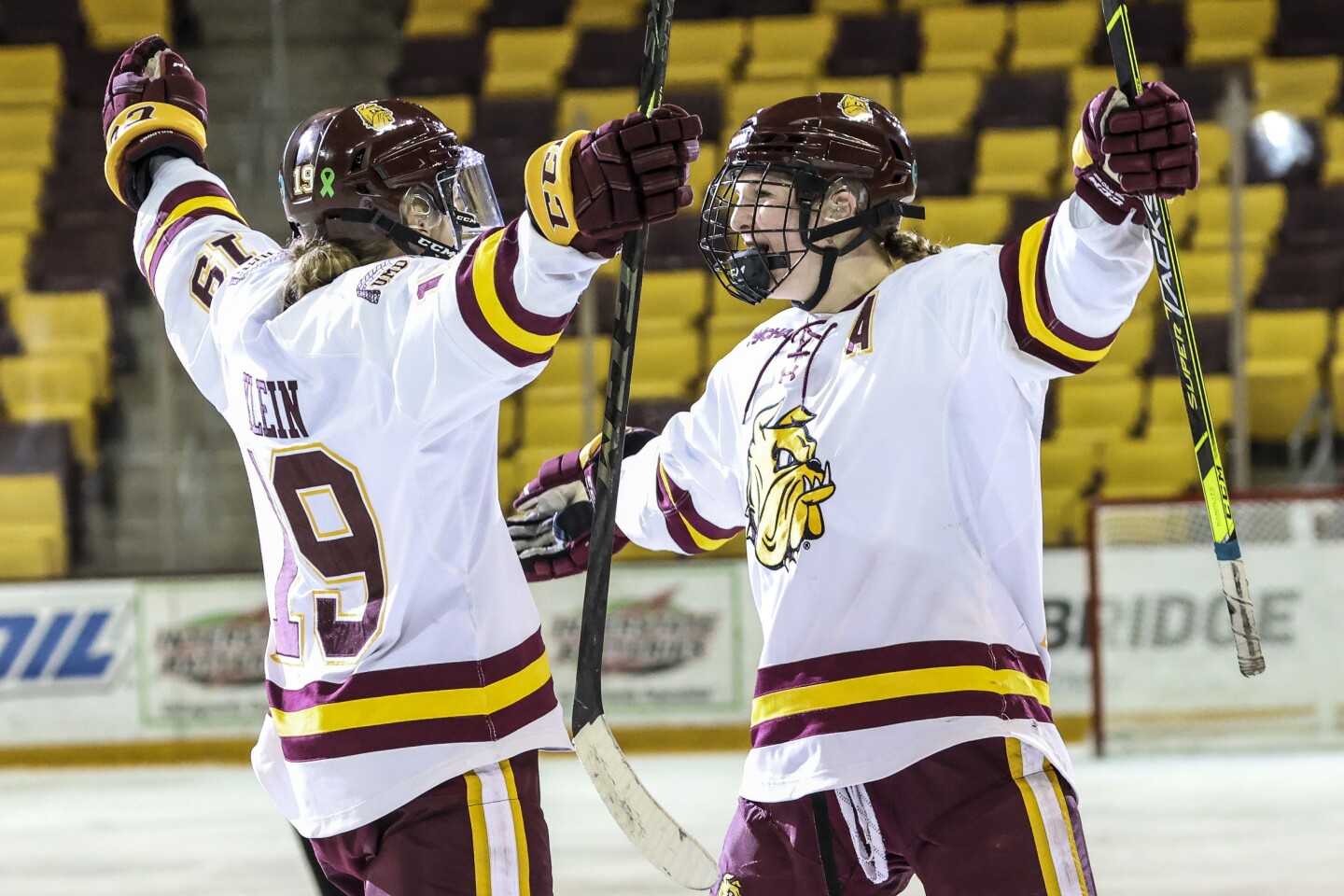 Women hockey players in purple and yellow compete against players in white and maroon at Amsoil Arena