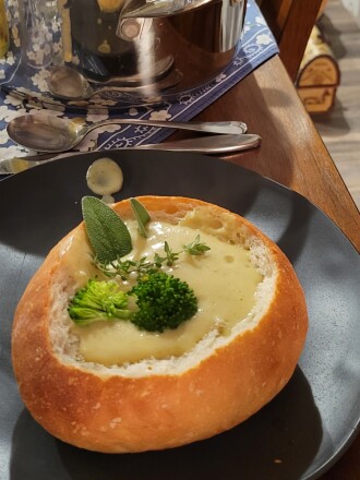 Yellow soup in bread bowl garnished with herbs and broccoli