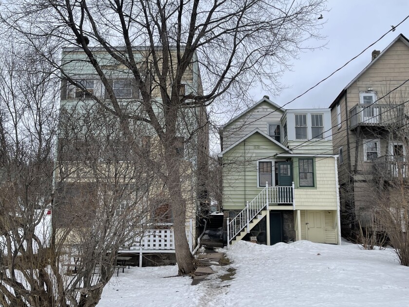 Rear view of two multi-family homes on snowy landscape, with trees and bushes in foreground.