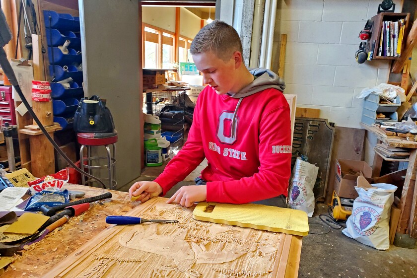 Boy sits in woodshop, sanding down door