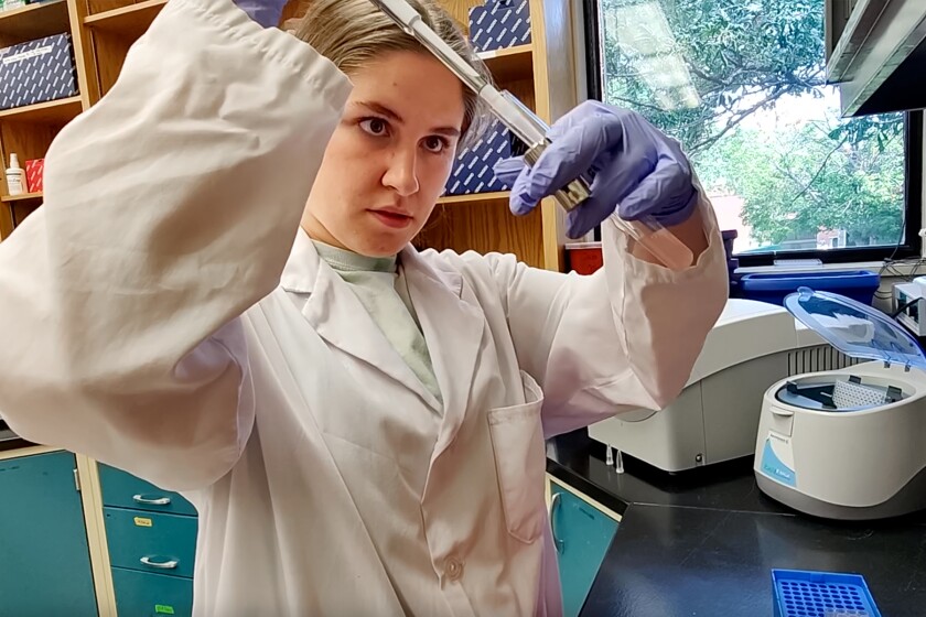 A woman in a lab coat uses a dropper.