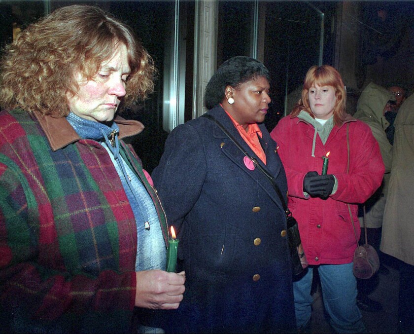 three women hold lit candles at vigil