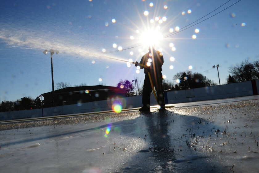 Against the sun, Scott Belisle with the Brainerd Parks and Recreation Department sprays water on one of the hockey rinks along Mill Avenue in Brainerd Thursday. With each application of water and freezing temperatures, coats of fresh ice are built up for the ice skating season. Brainerd Dispatch/Steve Kohls