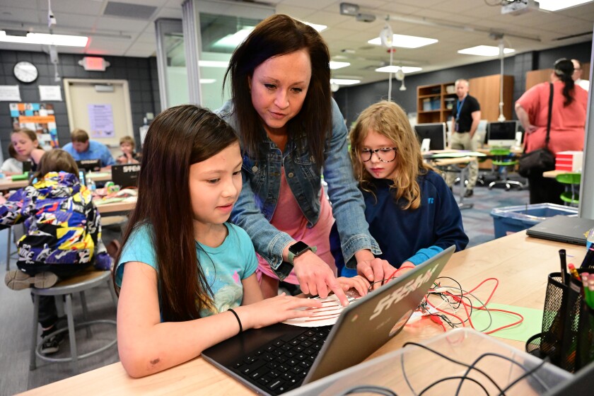 Allison Larsen stands between two students, using a computer.