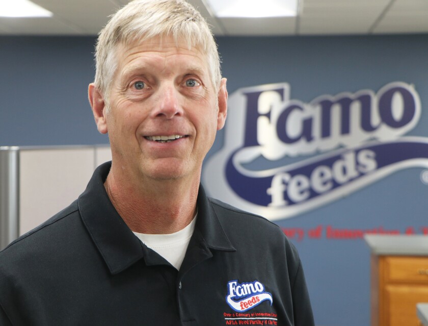 Famo Feeds owner John Beste stands against a company wall banner in an office corridor.