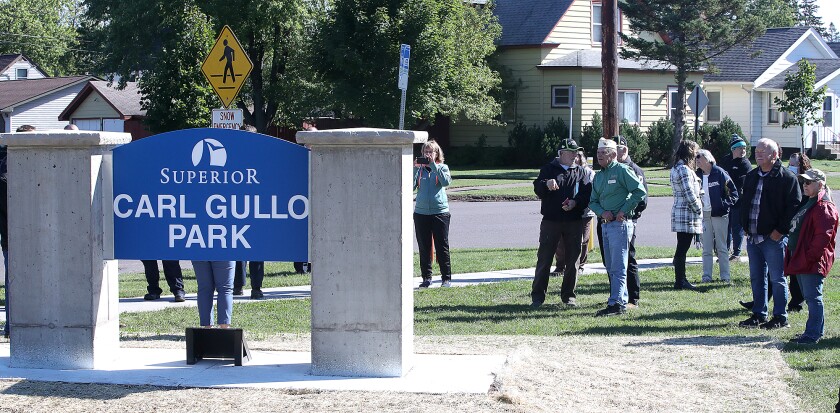 People gather near the new sign at Carl Gullo Park after a ceremony at the park on East 5th Street