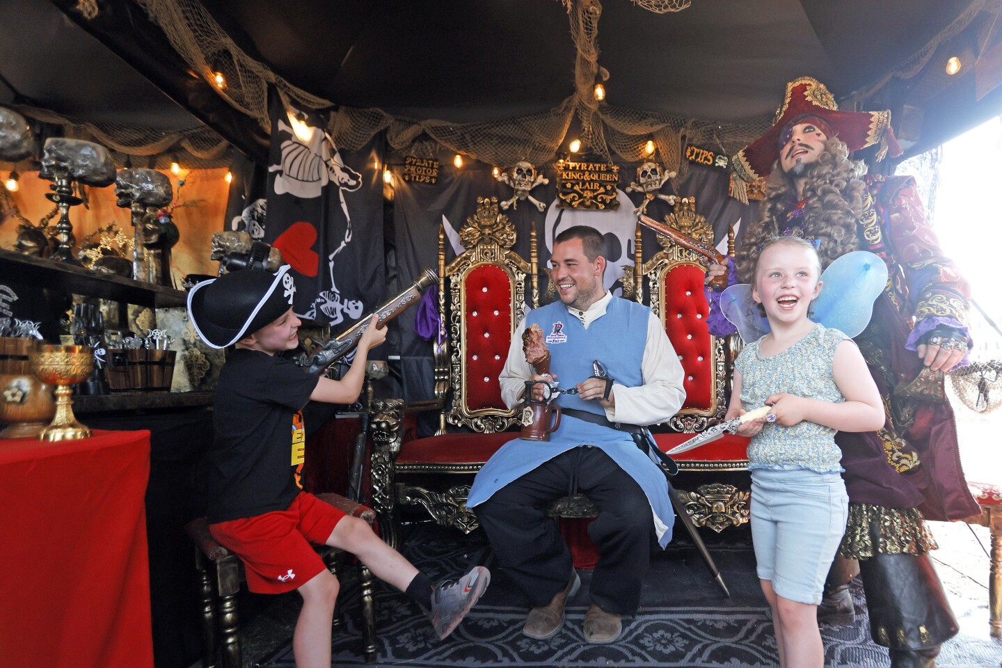 Man and two children smile with a pirate inside a pirate themed tent during a Renaissance Fair.