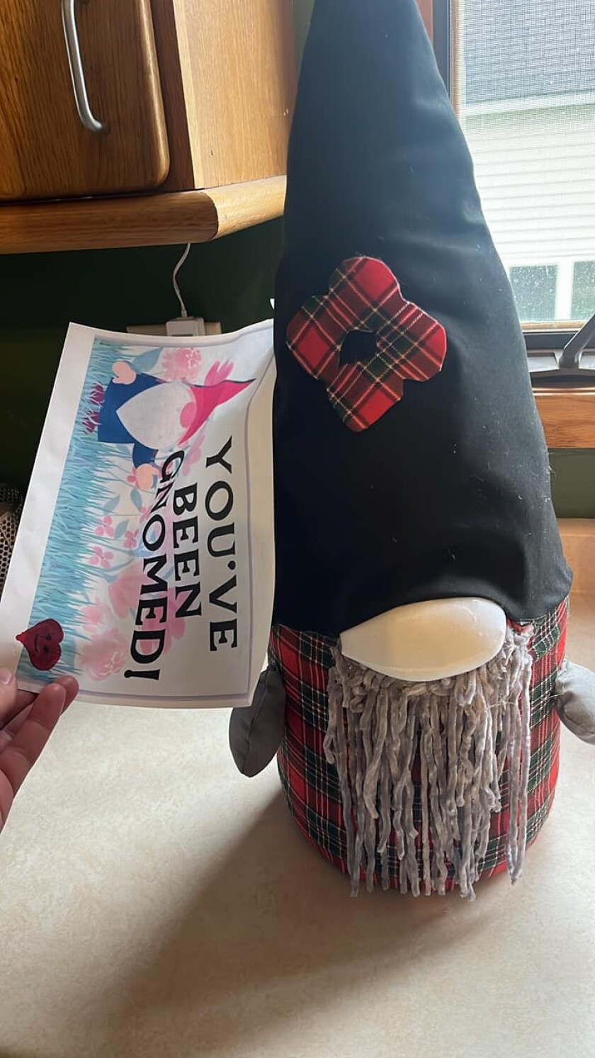 A small gray beareded gnome sits on a table with a note reading "You've been gnomed!"