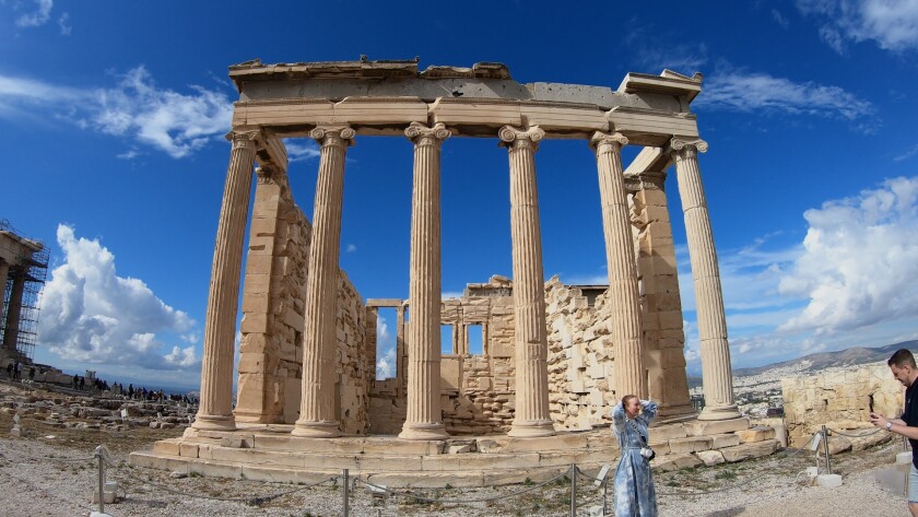 A columned structure at the Acropolis in Athens, Greece, tower over a woman posing for a photo.