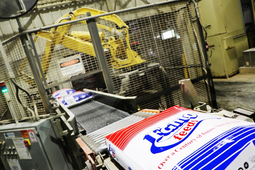 A yellow robot prepares to stack red-white-and-blue sacks of livestock feed.