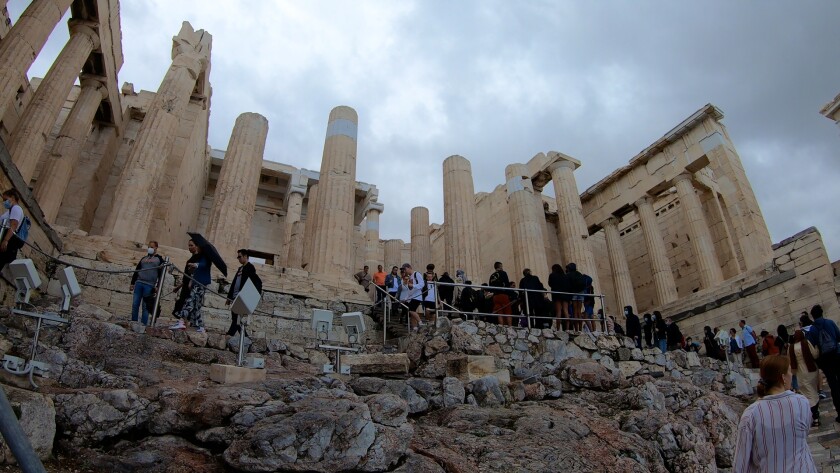 Tourists line up on the stairs leading up to the Acropolis, which is in the background.