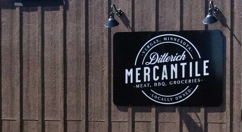 A black sign on the side of a wooden wall says, "Ditterich Mercantile. Vergas, Minnesota. Meat, BBQ, Groceries. Locally owned."