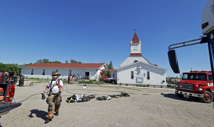 Several firefighters stand outside a small white church.