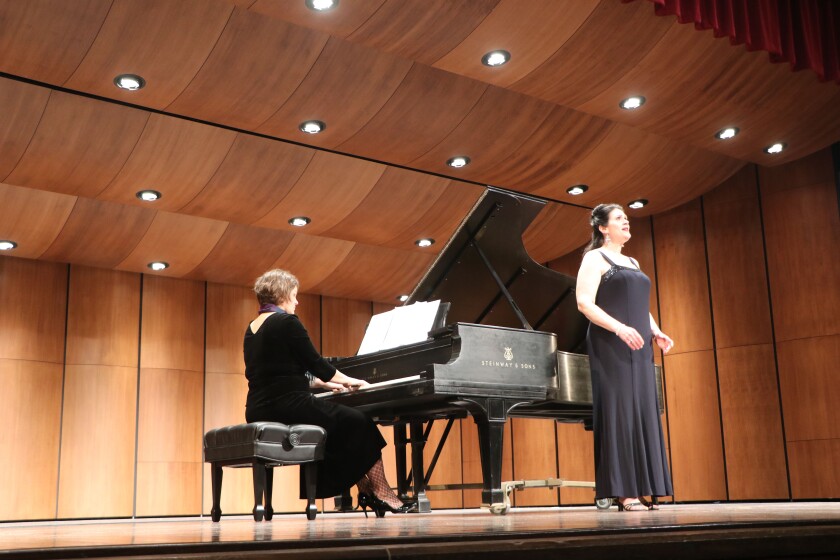 Anne Waltner plays at a Steinway grand piano on a college auditorium stage, as Marla Fogderud, a soprano soloist an associate professor of music at Northern State University, performs a recital.