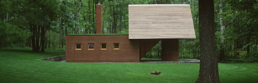 Small building has rectangular brick structure at left, with four small windows; to right is raised triangular structure supported by curved brick wall.