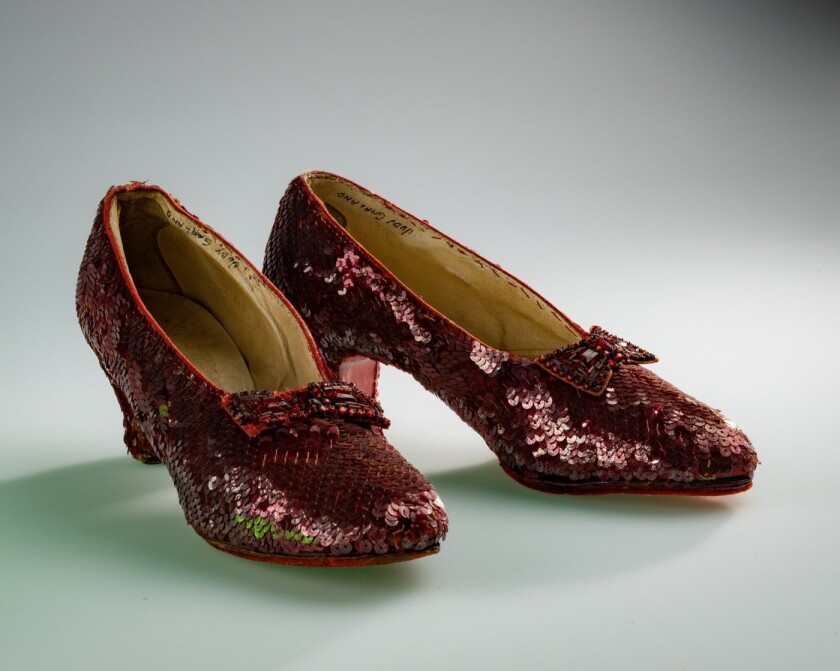 Pair of vintage red sequined shoes with a small heel, featuring decorative bows on the front. The shoes are reminiscent of a classic, iconic design