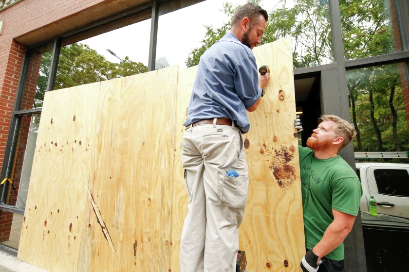 Michael Sciortino, the maintenance engineer for New South Properties, left, and Mark Neveu, a handyman with Indian Trail Service Company, attach wooden boards Thursday to broken windows on a building that was damaged during riots following a police shooting in Charlotte. REUTERS/Jason Miczek