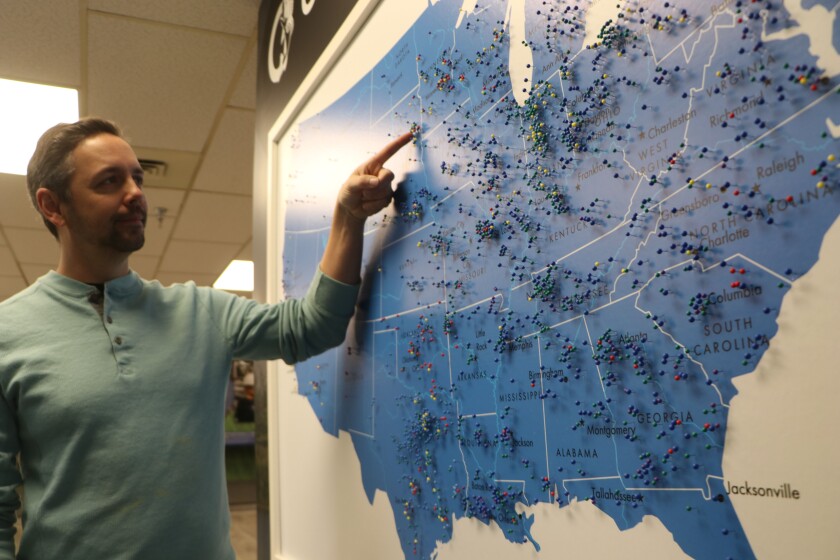 A man points to a map of the U.S. where his company sells fish food for aquaculture. Many pins are in the South and Southeast.