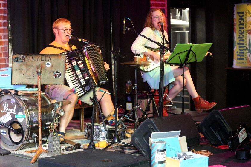 A man playing an accordion and singing and a woman playing a guitar and singing while on stage.