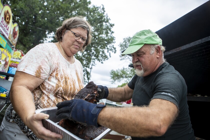 Becky Benoit, at left, holds a pan for husband Dave Benoit to place ribs into for their business, "The Holy Smoker," during the Kandiyohi County Fair on Saturday, August 13, 2022.