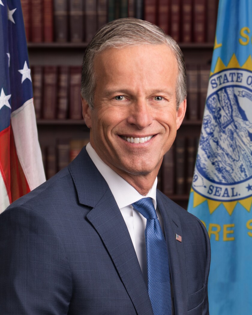John Thune sits in front of a bookshelf and the U.S. and South Dakota flags.